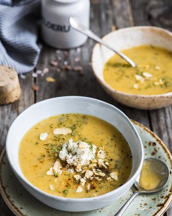 Auf dem Foto sind zwei Teller mit gelber Gemüsesuppe zu sehen. Die Suppen sind mit vielerlei Kräuter mariniert. | © SONNENTOR