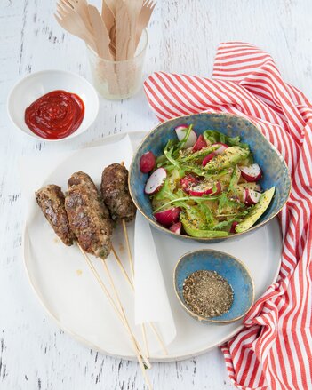 Auf dem Foto sind Spieße mit Cevapcici zu sehen. Daneben sieht man eine Schüssel mit Salat.  | © SONNENTOR