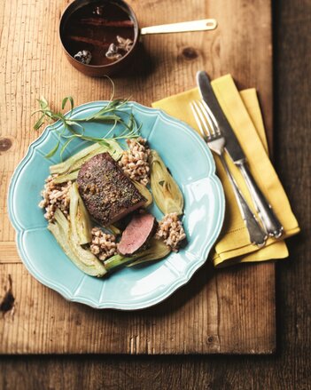 Auf dem Foto sieht man ein Teller mit einem Lammfilet auf Fenchel und Orangensauce. Dahinter sieht man eine Sauce und daneben liegt das Besteck. | © SONNENTOR