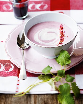 Foto von einer Tasse mit rosa Waldbeercreme. Die Creme ist mit rosa Blüten dekoriert und daneben ist Minze zu sehen. | © SONNENTOR