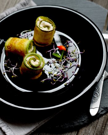 Auf dem Foto ist ein schwarzer Teller mit drei Stück Zucchinirollen gefüllt mit Feigenfrischkäse zu sehen. | © SONNENTOR