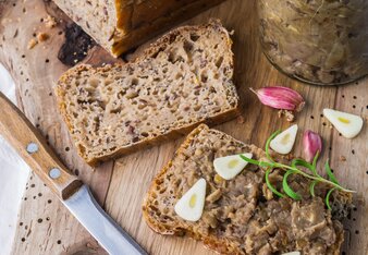 Auf dem Foto ist Brot zu sehen und daneben ein Glas Fenchel Alblinsen Aufstrich. Auf eine Brotscheibe ist der Aufstrich bereits gestrichen. | © SONNENTOR