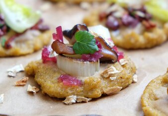 Foto von den Erdmandel Polenta Mini-Pizzen. Sie liegen auf einem Holztisch auf einem Backpapier. | © SONNENTOR