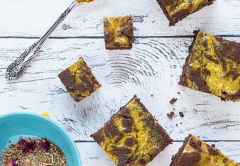 Auf dem Foto sind braun-gelbe Kurkuma Swirl Brownies zu sehen. Daneben liegt ein Löffel mit Kurkumapulver. | © SONNENTOR