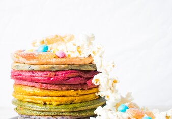 Auf dem Foto sind viel bunte Pancakes übereinander zu sehen. Von dem Turm aus Pancakes fallen Popcorn und Smarties herunter. | © SONNENTOR