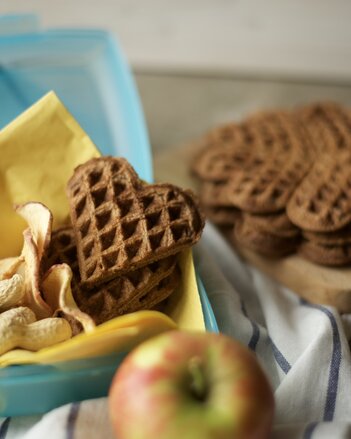 Auf dem Foto sind Schlaukakao Waffeln gemeinsam mit Erdnüssen in einer Jausenbox zu sehen. Im Hintergrund sieht man noch mehrere Waffeln. | © SONNENTOR