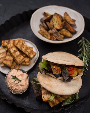 Auf dem Foto sieht man zwei Pita Brote mit Veggie Gyros. Im Hintergrund sieht man einen Teller mit Veggie Gyros und eine Schale mit Kartoffelwedges. | © SONNENTOR