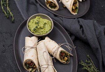 Auf dem Foto sieht man zwei Teller mit jeweils drei Stück Veggie Wraps darauf. Auf jedem Teller steht ein Schüsselschen Avocado Dip. | © SONNENTOR