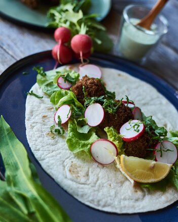 Auf dem Foto sieht man einen Wrap mit Wildkräuterfalafel, Salat und Radieschen zu sehen. Dahinter sieht man ein Gläschen mit Dip. | © SONNENTOR