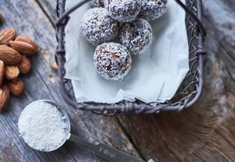 Auf dem Foto sind in einem Körbchen mehrere Espresso Energy Balls zu sehen. Daneben sind Mandeln und Kokosraspeln zu sehen. | © SONNENTOR