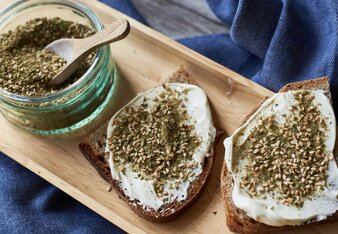 Auf dem Foto sieht man ein Gläschen mit Zatar. Daneben liegen zwei Scheiben Brot mit Aufstrich und Zatar darauf. | © SONNENTOR