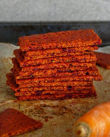 Auf dem Foto sind orange-rote Gemüsecracker zu sehen. Daneben liegt eine ganze Karotte. | © SONNENTOR