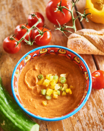 Auf dem Foto ist eine Schale mit klassischer Gazpacho zu sehen. Rundherum liegen Brot, Paprika, Tomaten und eine Gurke. | © SONNENTOR