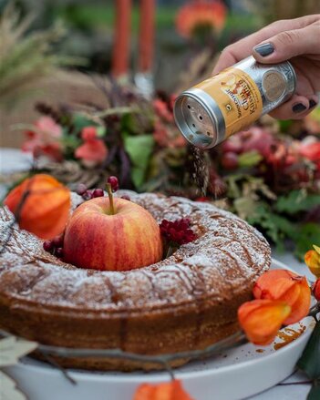 Auf dem Foto ist ein Apfel-Nuss-Kranz mit einem Apfel in der Mitte zu sehen. Rundherum ist herbstlich dekoriert. Der Kranz wird mi Chai-Küsschen bestreut. | © SONNENTOR