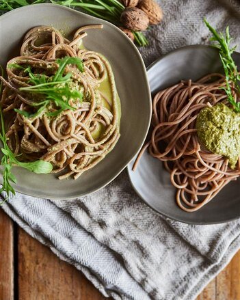 Auf dem Foto sind zwei Teller mit Buchweizennudeln mit Pesto zu sehen. Die Nudeln sind mit Rucola garniert. | © SONNENTOR