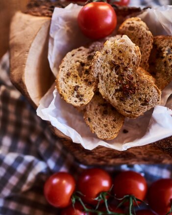 Auf dem Foto sind Brotchips mit Tomatenflocken-Öl in einem Körbchen zu sehen. Dahinter sieht man Tomaten. | © SONNENTOR