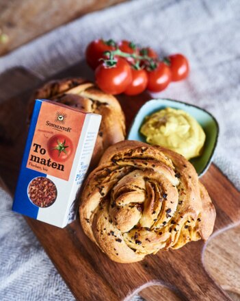 Auf dem Foto sieht man zwei Stück Tomaten-Swirl-Bread. Danben sieht man eine Schüssel mit Curry-Linsen-Dip. Auch eine Packung Tomatenflocken ist zu sehen. | © SONNENTOR