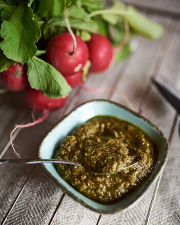 Auf dem Foto ist ein Schälchen mit Radieschengrün-Pesto zu sehen. Dahinter sind frische Radieschen zu sehen. | © SONNENTOR