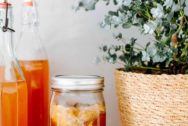 Auf dem Foto sieht man drei Flaschen mit Kombucha. Daneben sieht man ein Glas mit Kombucha mit Eis. | © SONNENTOR