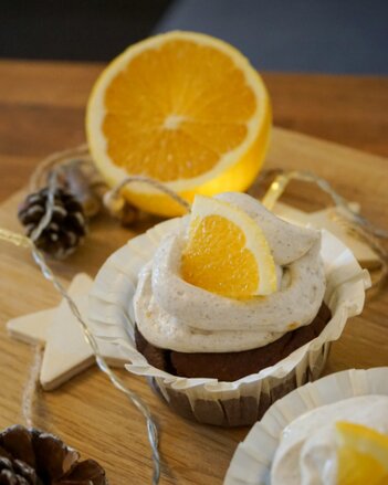 Auf dem Foto ist ein Cupcake zu sehen, der mit einer Creme und Orange verfeinert ist. Daneben sind Zapfen zu sehen. | © SONNENTOR