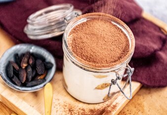 Auf dem Foto sieht man ein Glas mit Tiramisu. Auf das Tiramisu wird Zimt gestreut. Daneben sieht man eine Schüssel mit Tonkabohnen. | © SONNENTOR