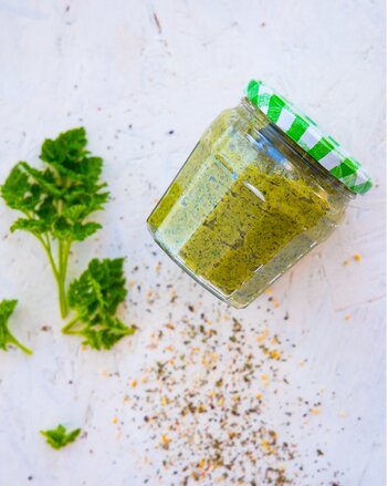 Auf dem Foto ist ein Glas mit Petersilien-Pesto zu sehen. Daneben sind Gewürze verstreut und auch frische Petersilie ist neben dem Glas zu sehen. | © SONNENTOR