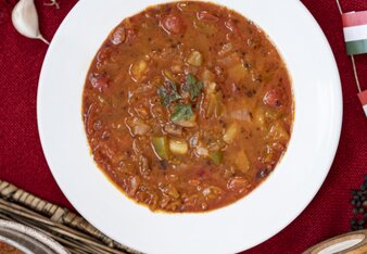 Auf dem Foto sieht man einen Teller mit ungarischer, veganer Gulaschsuppe. Daneben sieht man Paprika und Knoblach. | © SONNENTOR