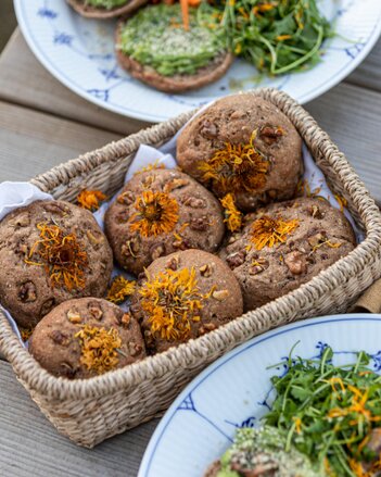 Auf dem Foto sind Walnuss-Brötchen mit Ringelblumen darauf zu sehen. Die Brötchen liegen in einem Korb. | © SONNENTOR