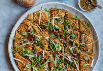 Der Kimchi Pancake ist als tellergroßer Pancake gebacken worden und in kleine Rauten geschnitten. Dekoriert ist er mit länglich geschnittenen Jungzwiebel Streifen und Sesam.  | © SONNENTOR