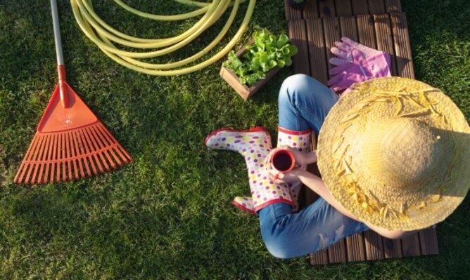 Auf dem Foto ist eine Frau zu sehen die mit einer Tasse Tee im Garten sitzt. Daneben sind ein Gartenschlauch, ein Rechen und Salatpflanzen zu sehen. | © SONNENTOR