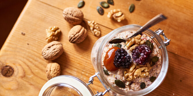 Auf dem Foto sieht man ein Glas mit Porridge. Getopped ist er mit zahlreichen Superfoods wie Kürbiskerne, Walnüsse und Brombeeren. | © SONNENTOR