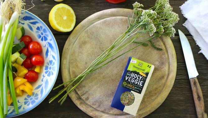 Auf dem Foto ist ein Holzbrett mit einer SONNENTOR Packung Holy Veggie zu sehen. Daneben steht eine Schüssel mit frischem Gemüse. | © SONNENTOR