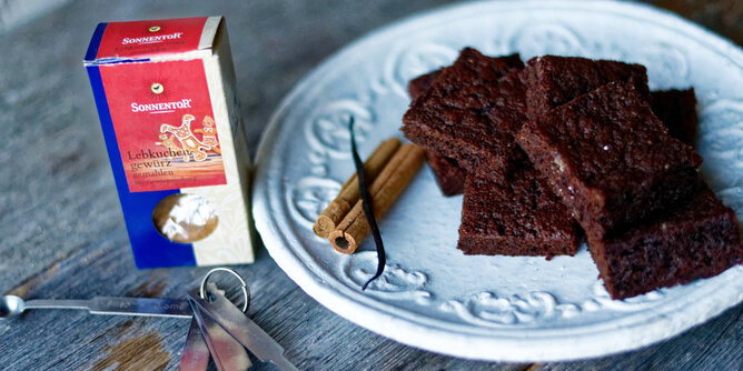 Auf dem Foto sieht man einen Teller mit Lebkuchenbrownies. Daneben liegt eine Zimtstange. Auch eine Packung Lebkuchengewürz ist zu sehen. | © SONNENTOR