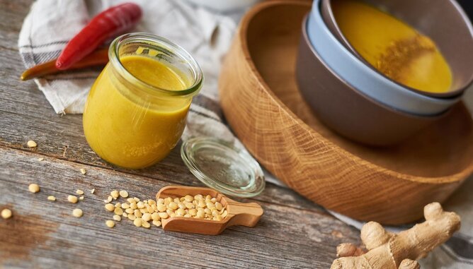 Auf dem Foto sieht man einen Teller mit gelber Linsensuppe. Daneben sieht man frischen Ingwer, Linsen und Paprika. | © SONNENTOR