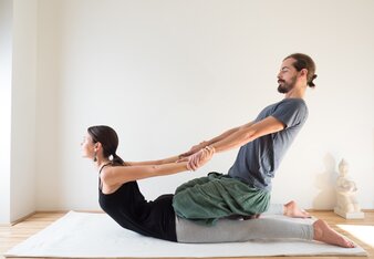 Foto von einer Frau in der Yogaposition die Kobra. Ihr Yogapartner unterstützt sie dabei. | © SONNENTOR