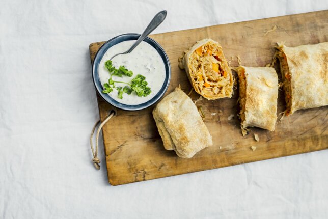 Auf dem Foto ist ein Brett mit Sauerkraut-Kimchi-Strudel zu sehen. Daneben steht eine Schale mit Dip. | © SONNENTOR